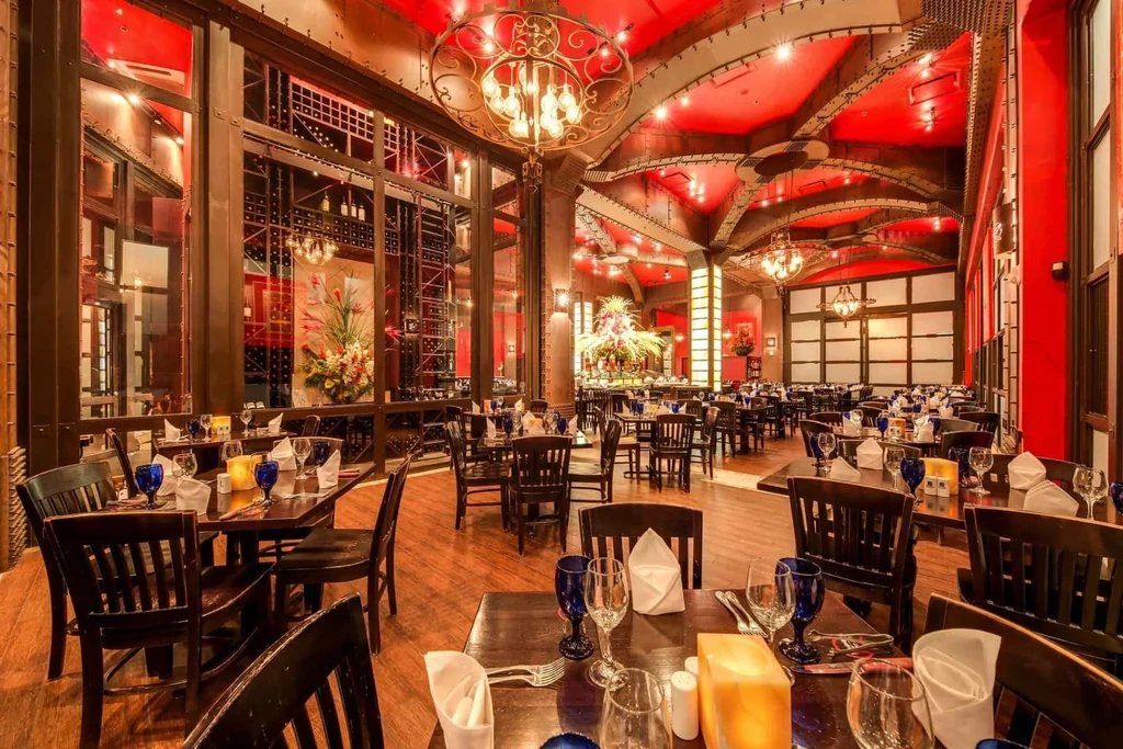Empty upscale restaurant with dramatic red ceiling, chandeliers, and set tables.
