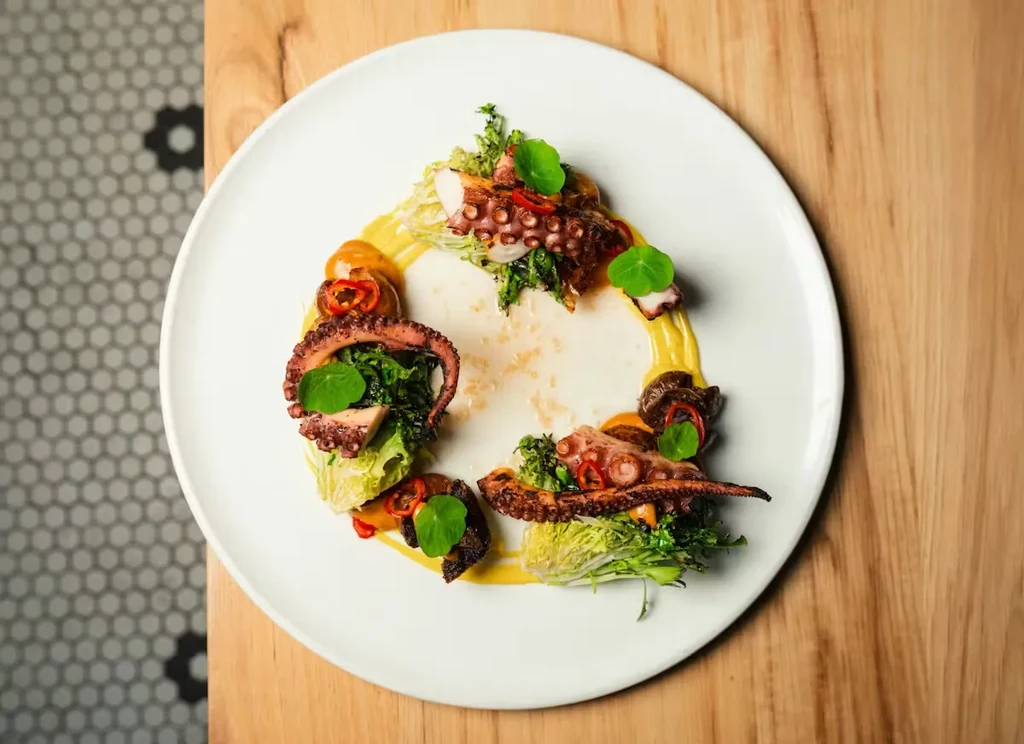 Plated dish of seared octopus, greens, chili, and yellow sauce.