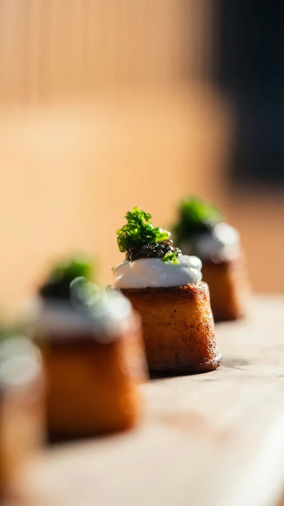 Three canapés with golden base, caviar, cream, and green herbs.