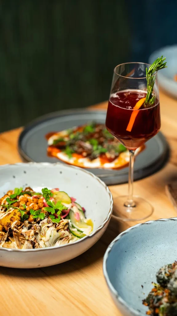 Vibrant salad bowl, dark red cocktail, and other dishes on wood table.