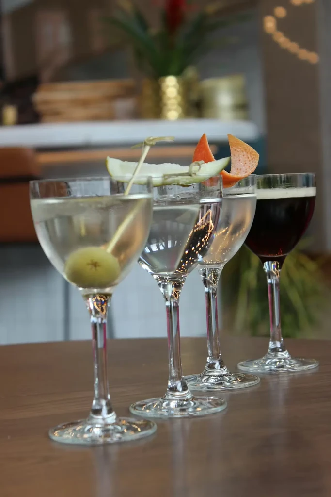 Four different beverages in stemmed glasses on a wooden table.