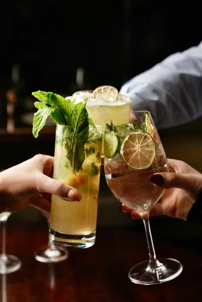 Three garnished cocktails held by hands in a celebratory toast.