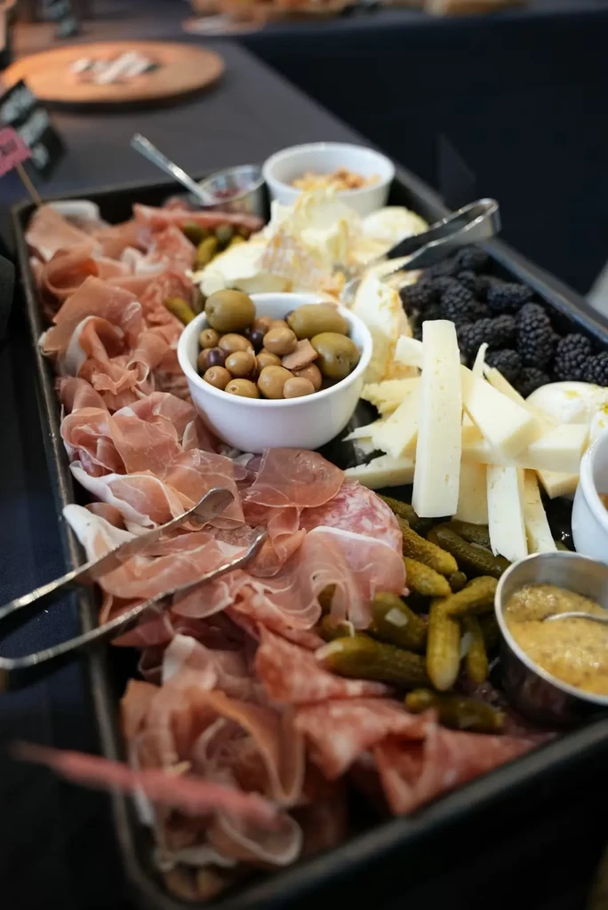 Large platter of charcuterie, cheeses, olives, blackberries, and tongs.