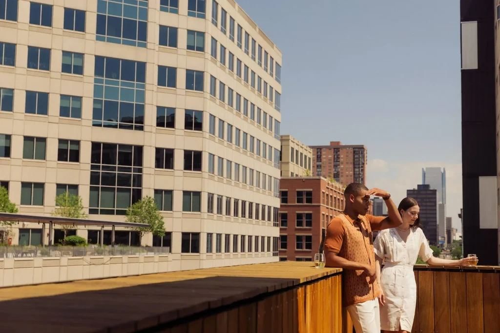 Man and woman drinking on a sunny city rooftop with cityscape.