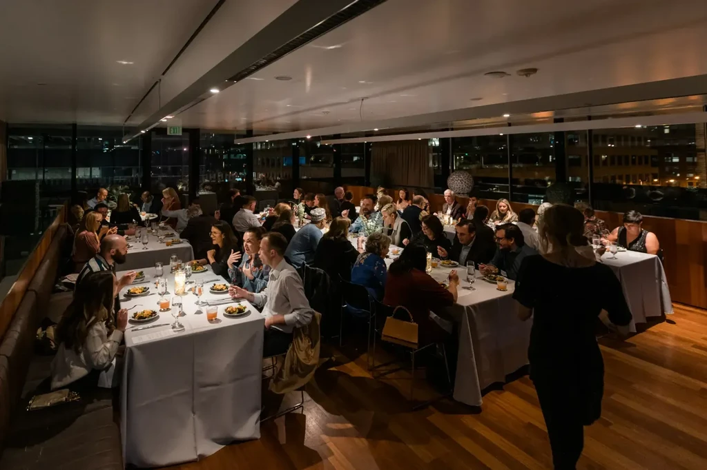 Warmly lit, elegant restaurant dining room, busy with diners at night.
