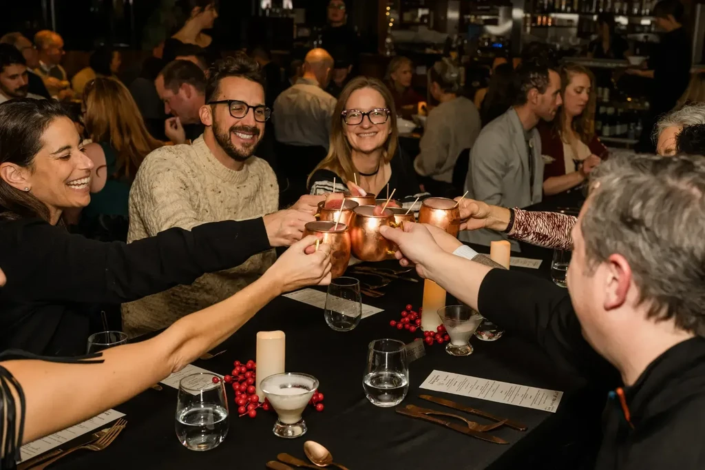 Smiling group toasting with copper mugs at a candlelit restaurant table.