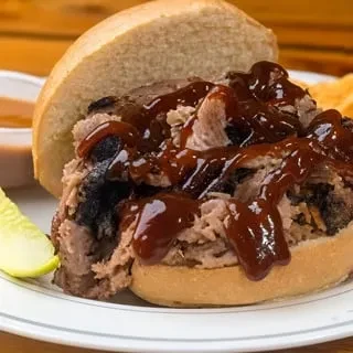 Large pulled pork sandwich, open-faced, with glossy BBQ sauce, pickle.