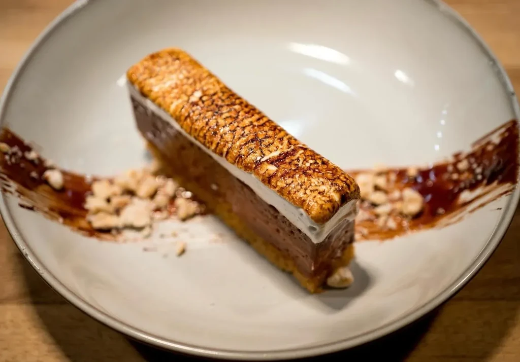 Brûléed layered dessert slice with dark sauce and crunchy garnish.