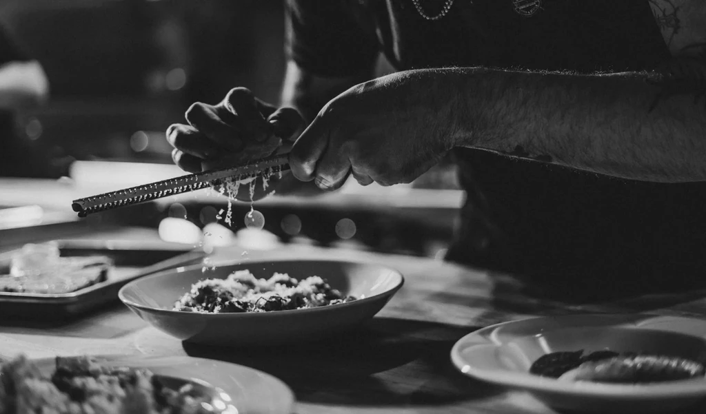 Black and white close-up of hands grating food over a bowl.