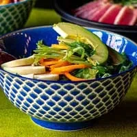 Blue bowl of colorful poke, avocado, and red fish on green surface.