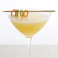 Pale yellow cocktail in martini glass, garnished with red and green chilies.