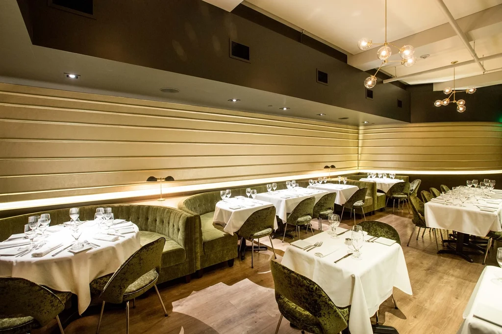 Restaurant interior with green velvet seating, ribbed gold walls, modern chandeliers.