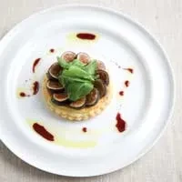 Fig tart with sliced figs, green leaves, dark sauce, and olive oil.