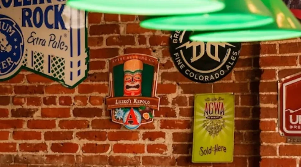 Rustic brick wall adorned with various branded beer and brewing signs.
