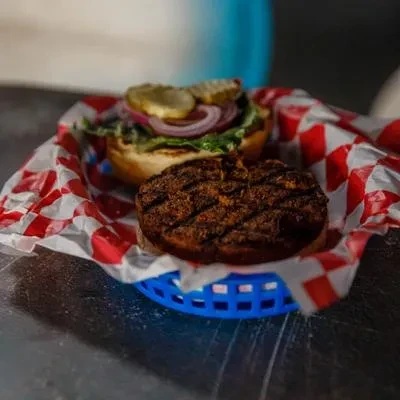 Open-faced grilled burger with lettuce, onion, pickles in a blue basket.