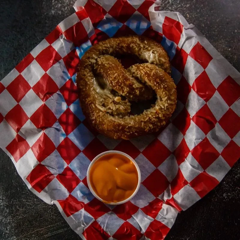 Pretzel covered in melted cheese, served with a cup of cheese sauce.