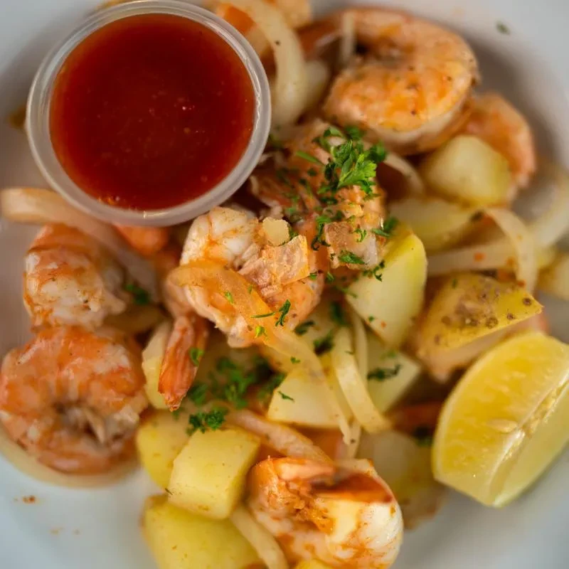 Cooked shrimp, potatoes, and onions with dipping sauce and lemon.