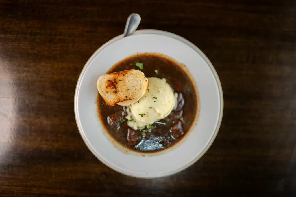 Dark stew topped with mashed potatoes, green herbs, and baguette.