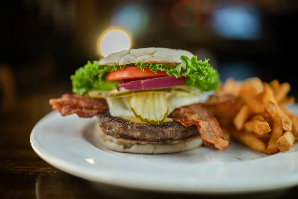 Stacked bacon cheeseburger with golden french fries on a white plate.