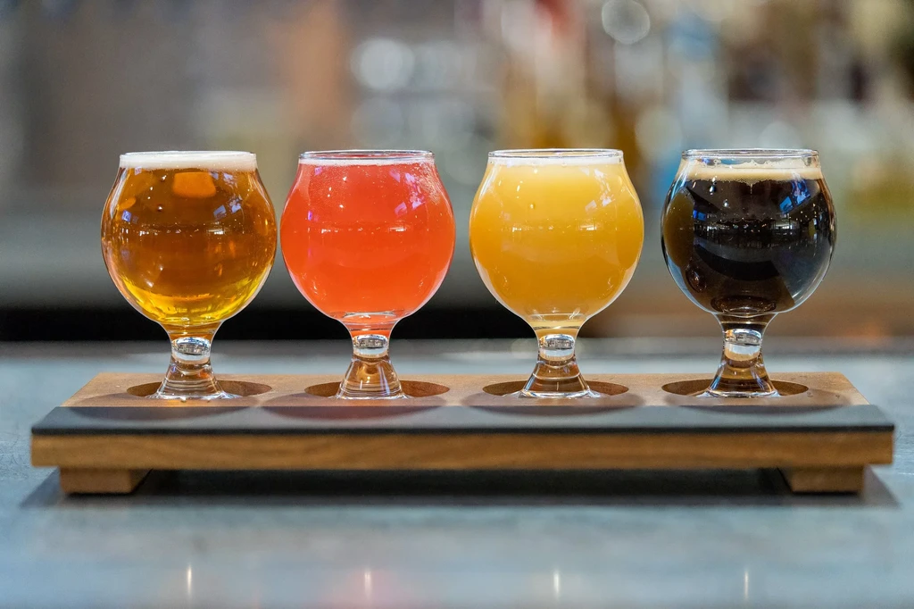 A flight of four distinct craft beverages on a dark wooden paddle.