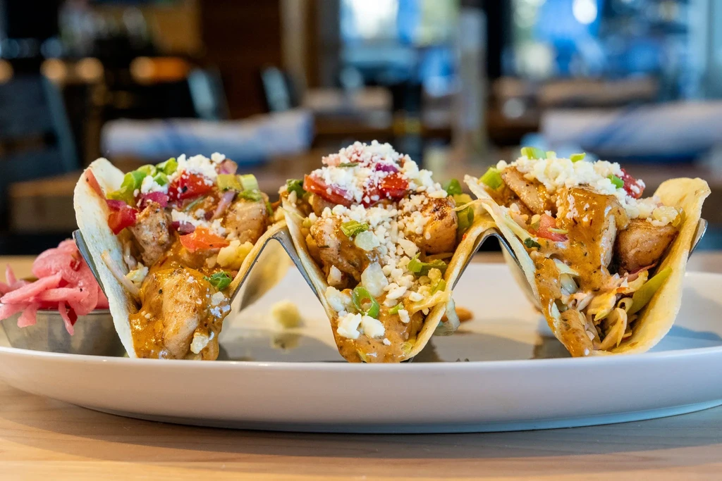 Three tacos on stands with abundant fillings and pickled onions.