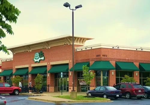 Brick commercial building with green awnings, turtle logo, and parking lot.
