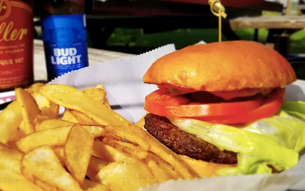 Burger, wedge fries, and beer bottles on a blurred outdoor picnic table.