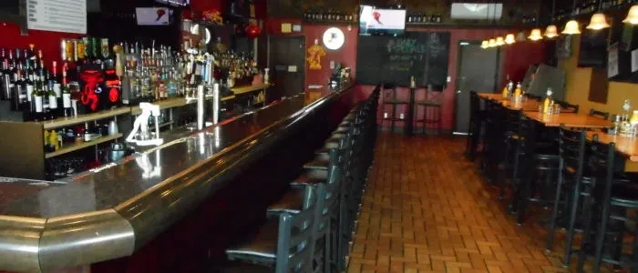 Empty, dimly lit bar interior with a long counter, stools, and tables.