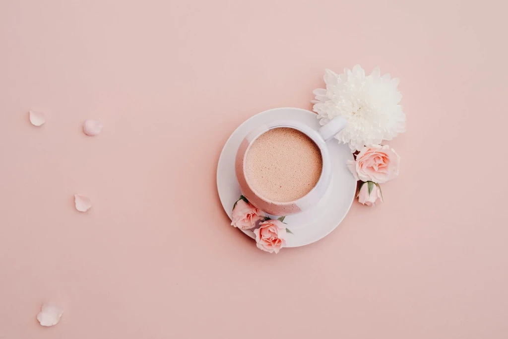 White cup of frothy drink on saucer with pink and white flowers.