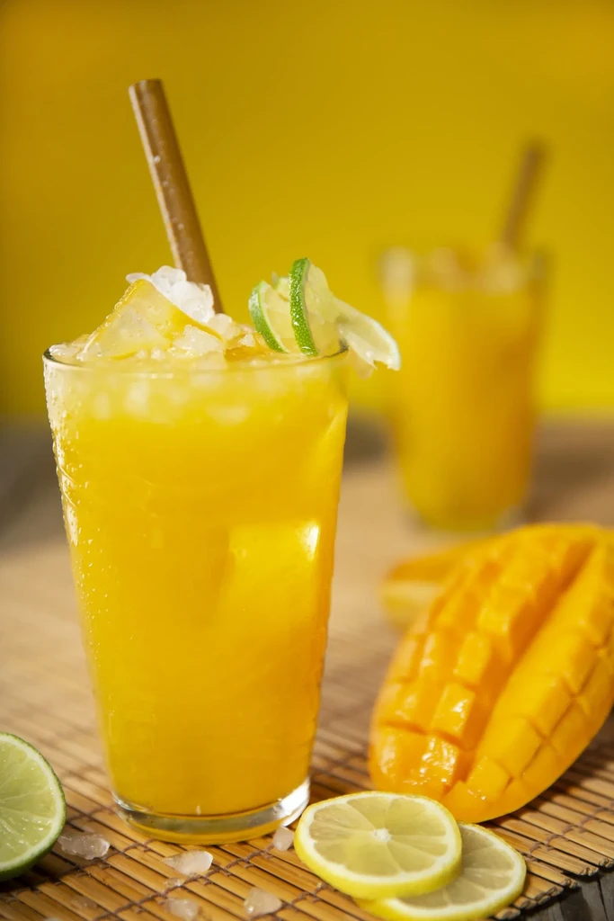 Yellow drink with crushed ice, lime, mango, and lemon on a mat.