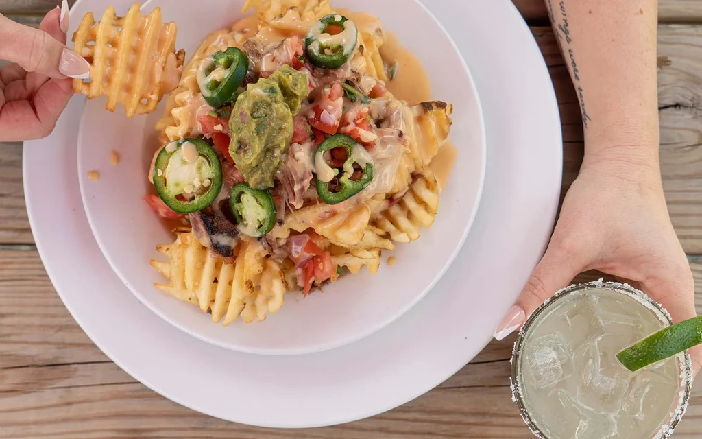 Overhead: Loaded waffle fries with cheese, meat, guacamole, and a margarita.
