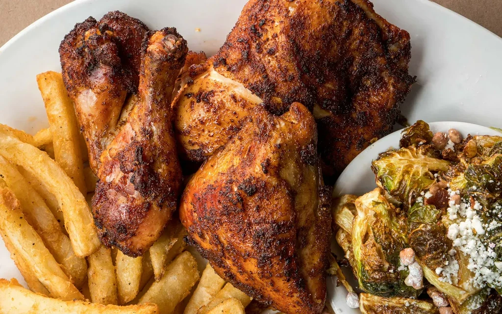 Plate of roasted chicken, fries, and brussels sprouts topped with cheese.