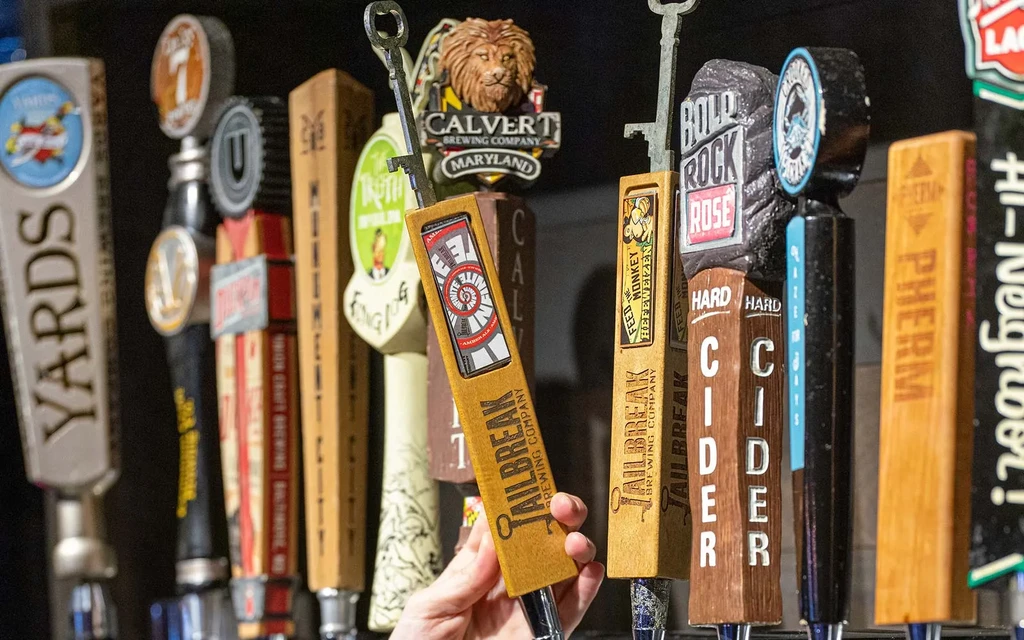 Many diverse beer and cider tap handles, one held by a hand.