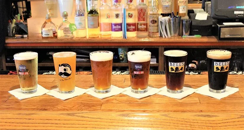 A row of six different beers with logos on a bar.