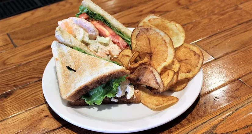 Diagonally cut sandwich with creamy salad, tomato, and potato chips.