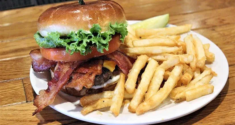 A bacon cheeseburger, french fries, and a pickle spear.