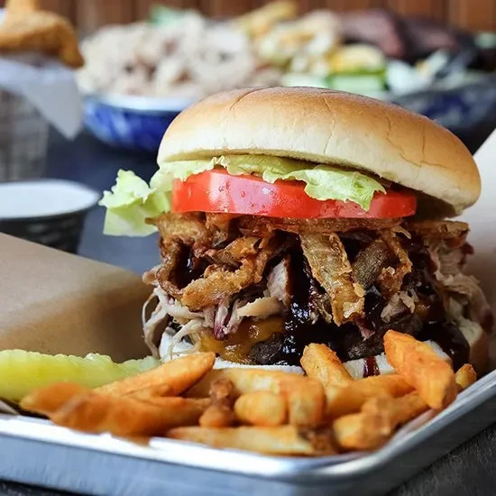 Pulled meat burger, fries, and pickle spear on a metallic tray.