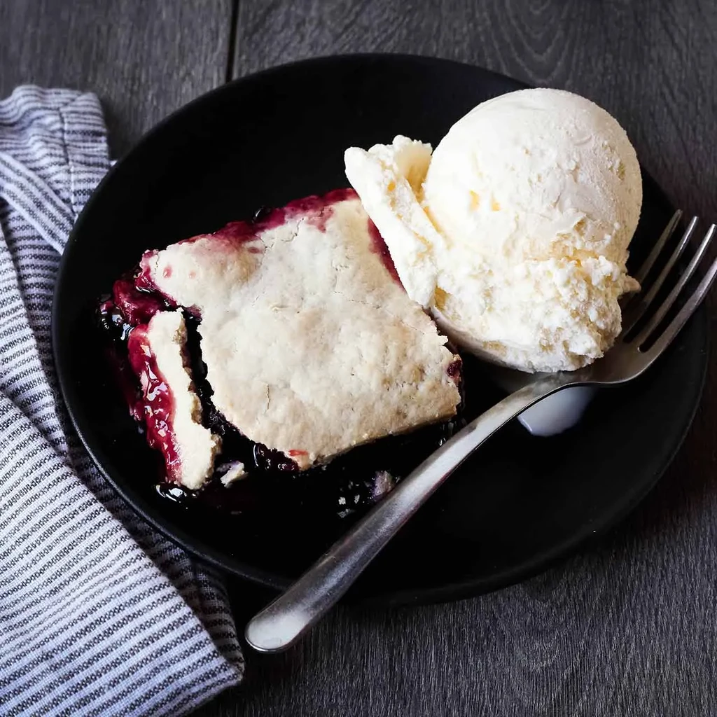 Rustic berry pie slice with melted vanilla ice cream on a plate.