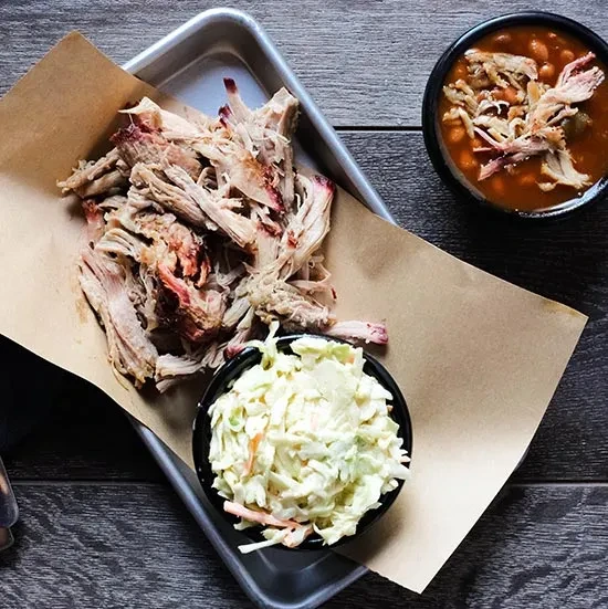 Rustic pulled pork meal in a metal tray with coleslaw and beans.