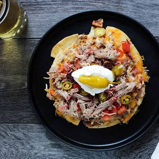Close-up of loaded nachos with meat, cheese, tomatoes, jalapeños, sour cream.