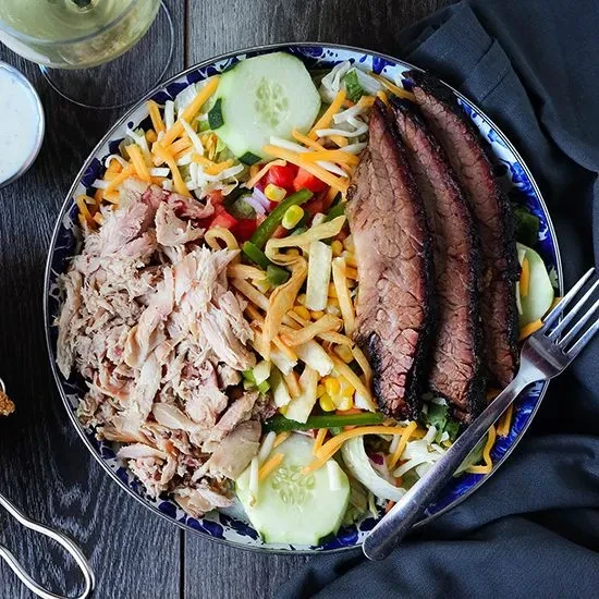 Overhead view of a colorful salad with two meats and vegetables.