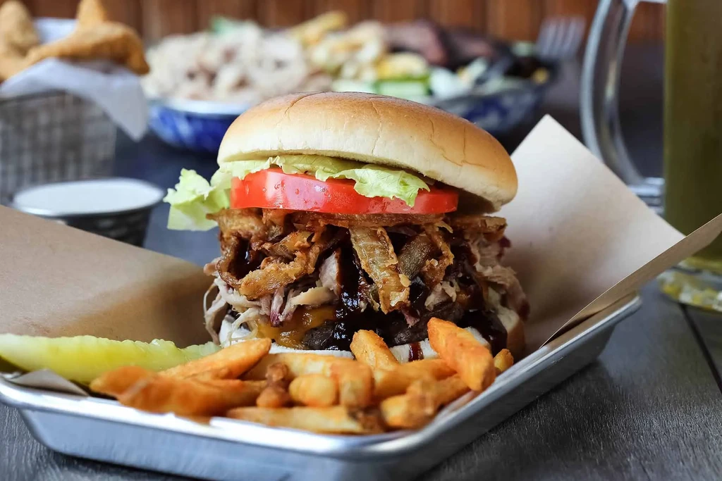 Complex gourmet burger, french fries, and pickle on a metal tray.