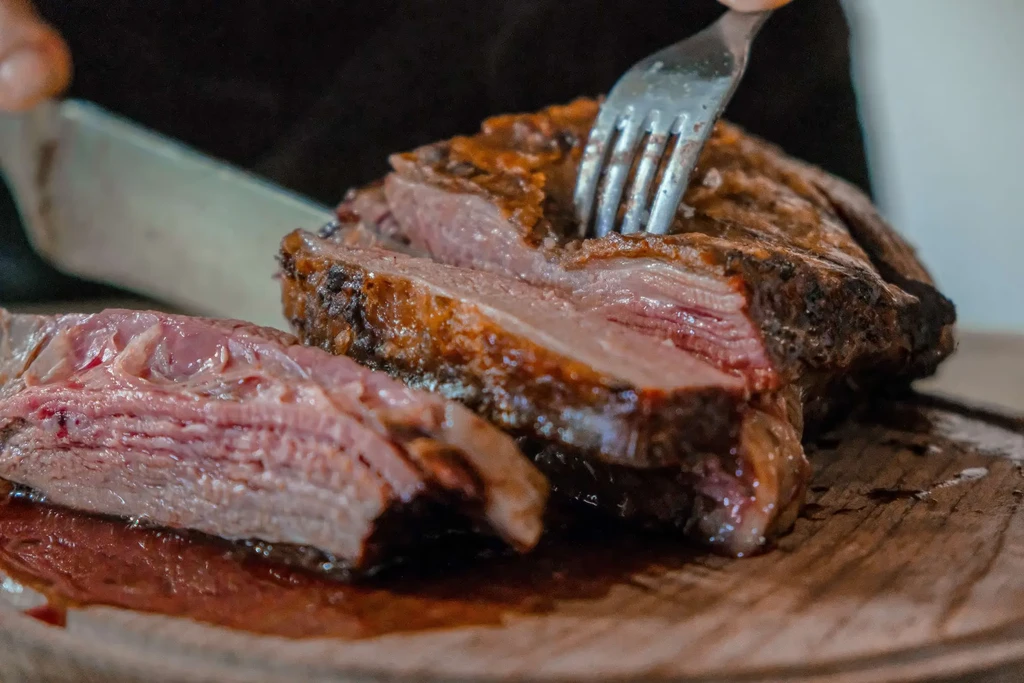 Hands slicing medium-rare roasted beef on a wooden board.