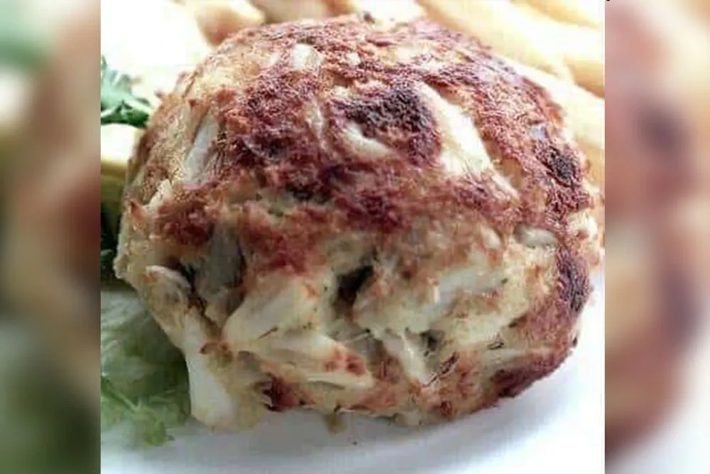 Close-up of a golden-brown crab cake with flaky meat and green garnish.
