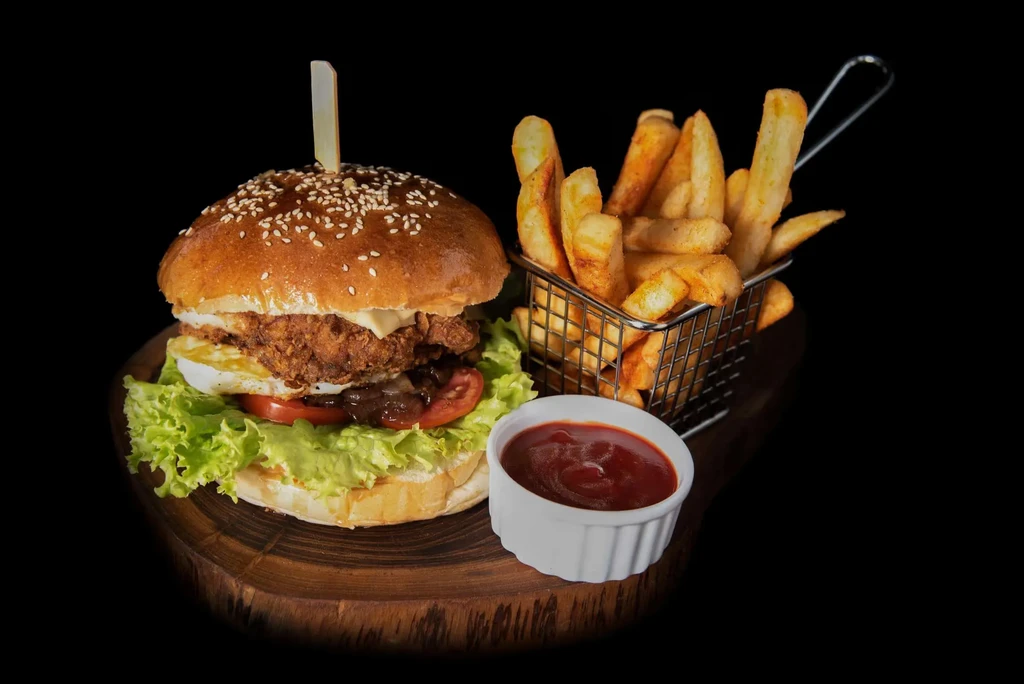 Stacked burger, fries, and ketchup served on a dark wooden board.