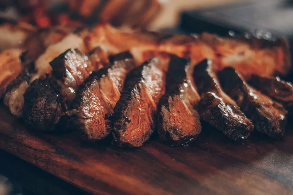 Thick slices of medium-rare beef with seared crust on a wooden board.