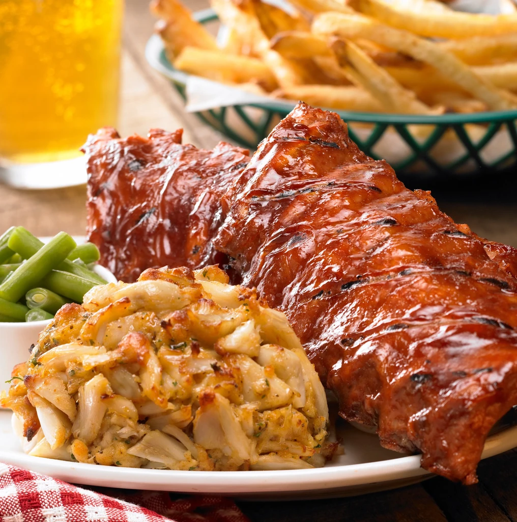 Close-up of barbecue ribs, crab cake, green beans, fries, beer.