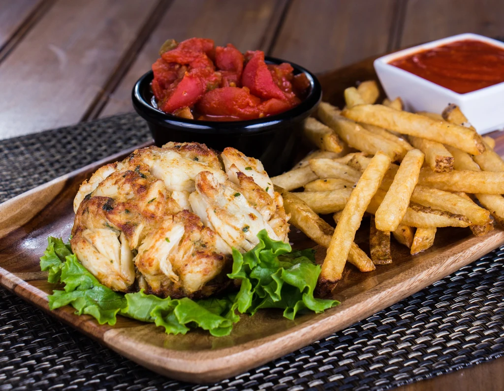 Crab cake, french fries, and two sauces on a rustic wooden platter.