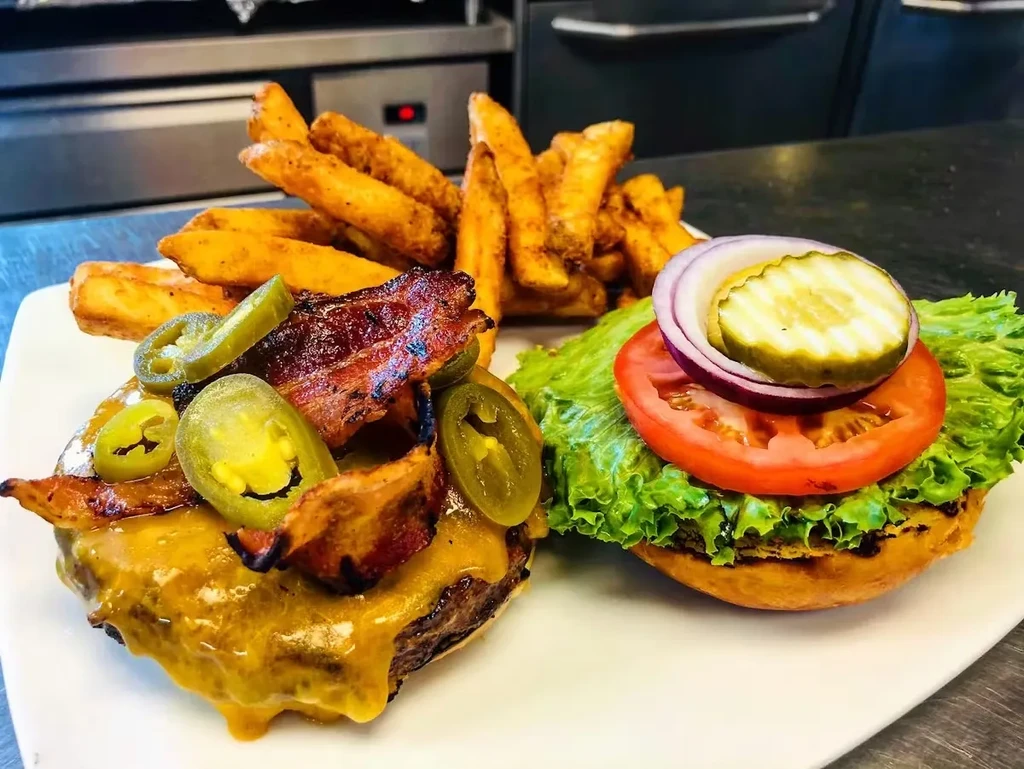 Open-faced gourmet burger with fries, bacon, cheese, and jalapeños.