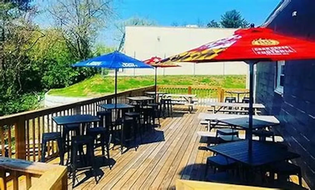 Sunny wooden deck with seating, branded umbrellas, and green foliage.